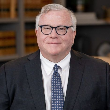 A man in a suit and tie is standing in front of a bookshelf.